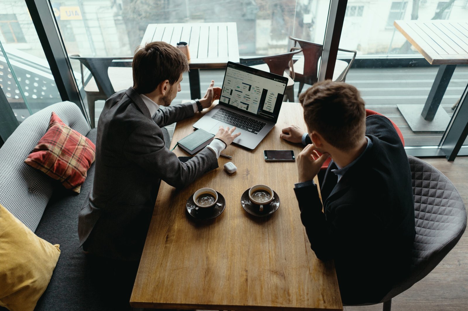 Two businessmen talking about new opportunities sitting with laptop at desk, planning project, considering business offer, sharing ideas while drinking coffee together