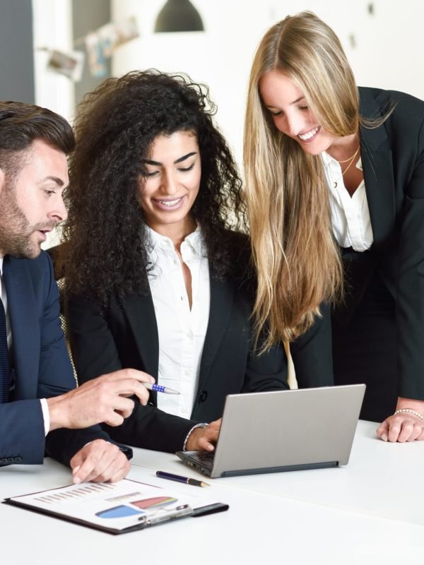 Multi-ethnic group of three businesspeople meeting in a modern office. Two women and a caucasian man wearing suit looking at a laptop computer.